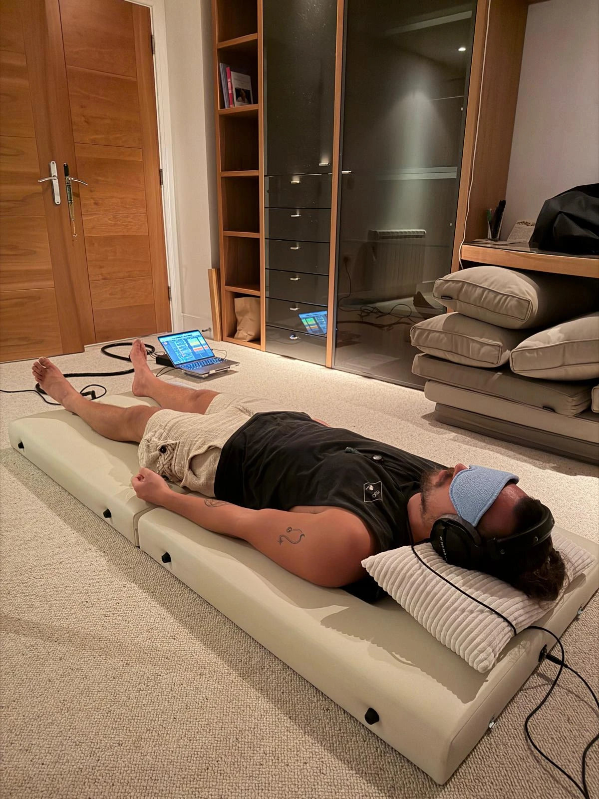 A person lying on the Onizion sound bed, wearing studio headphones and an eye mask
