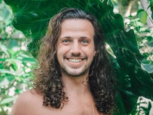 Jake Delmonte smiling in front of large green leaves